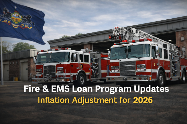 Two fire trucks parked outside a brick fire station, with the Pennsylvania state flag on the left. Overlaid text reads “Fire & EMS Loan Program Updates – Inflation Adjustment for 2026.”.
